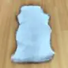 Messenger_creation_AD1863FF-B153-42C4-BA46-A7BF0B5D4CB8 White sheepskin rug with fluffy brown edges laid on a wooden floor