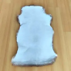 White sheepskin rug with fluffy brown edges laid on a wooden floor